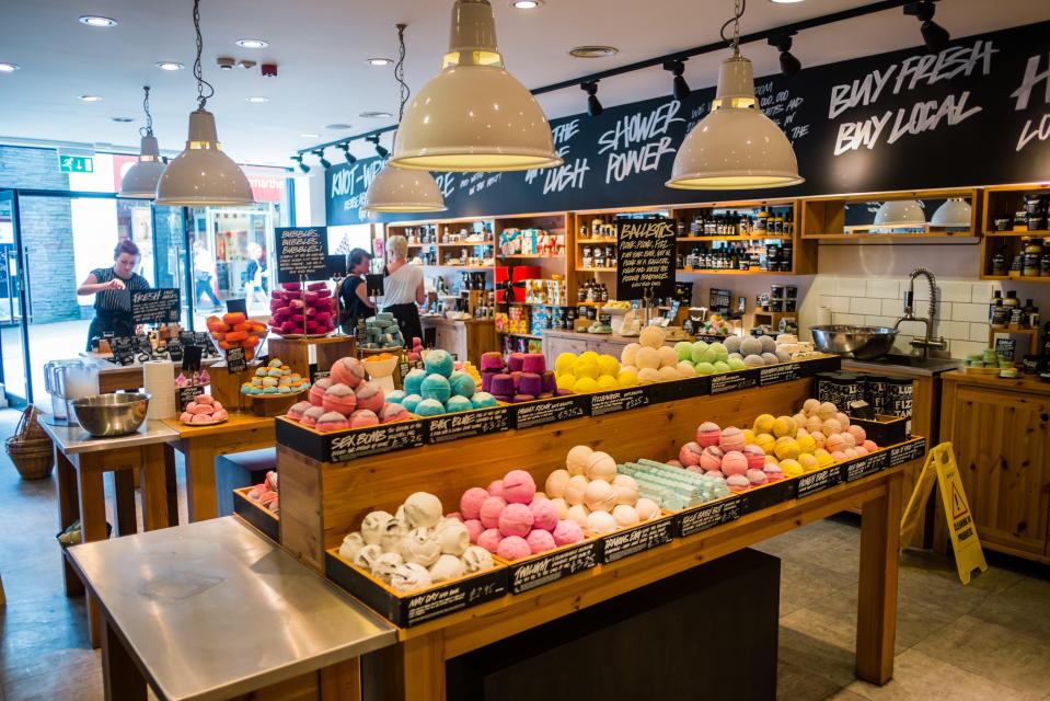 Interior of a Lush Cosmetics shop with tables piled high with colorful bath bombs and soaps.