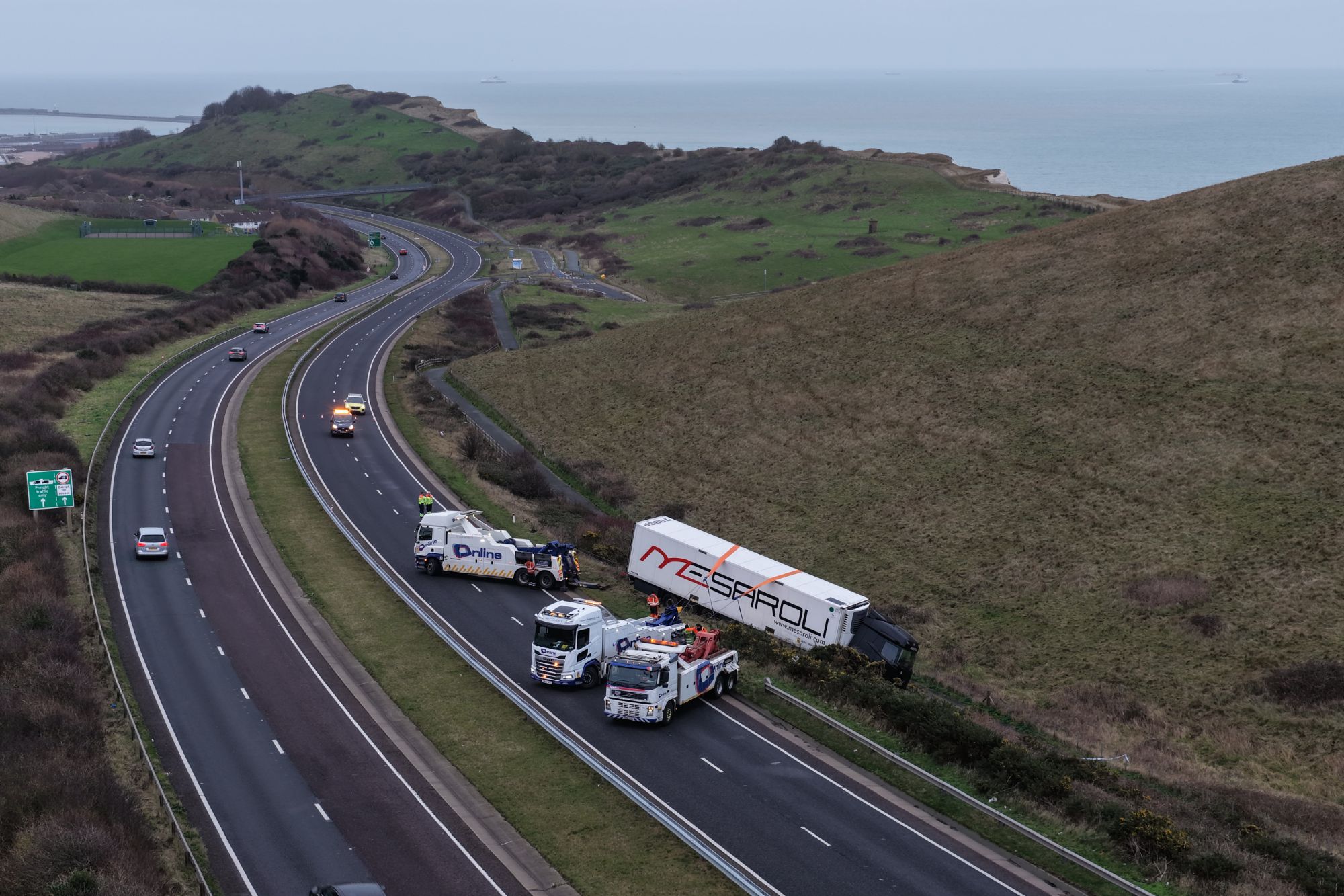 An image collage containing 1 images, Image 1 shows An overturned HGV (Heavy Goods Vehicle) on the side of a highway near Dover, with recovery vehicles on the road