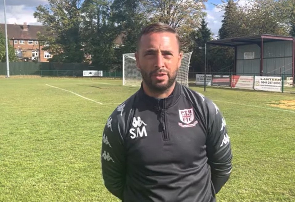 A man in a black and grey long-sleeved shirt with the "PTH FIC" logo standing on a soccer field.