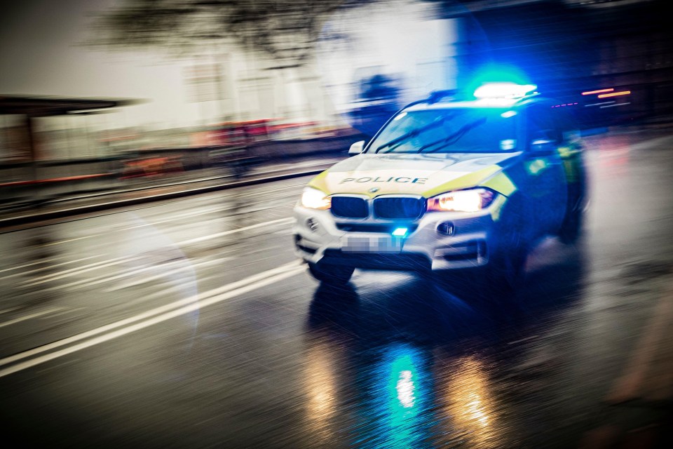 A police car with flashing blue lights speeding down a wet road.