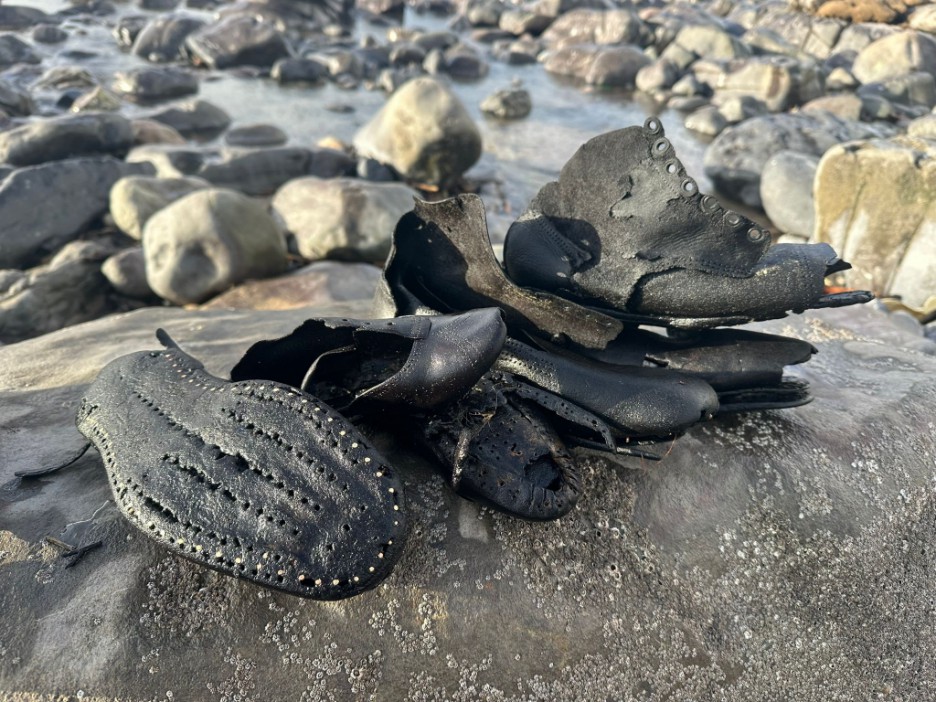 Pile of water-damaged Victorian shoes, including a boot and a flat shoe with studded sole, found on a rocky beach.
