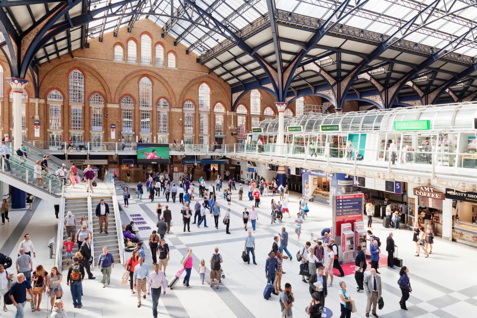 A bustling Liverpool Street Station in London, with many people, shops, and escalators.