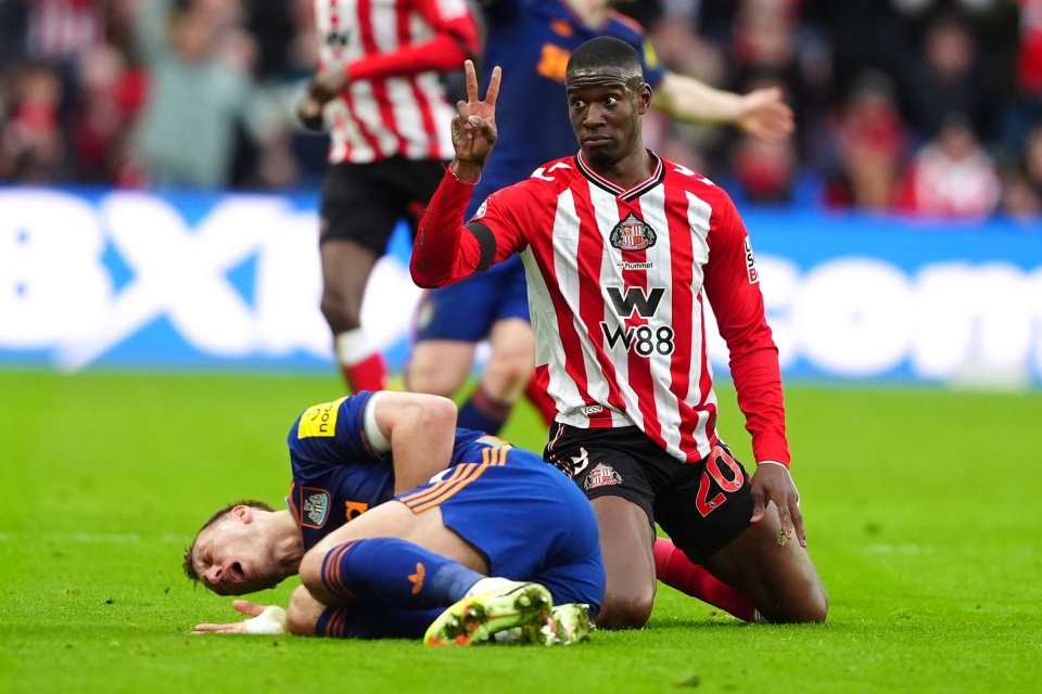 Sunderland player in red and white kneeling next to an injured Newcastle United player in blue, who is lying on the ground holding his ribs.