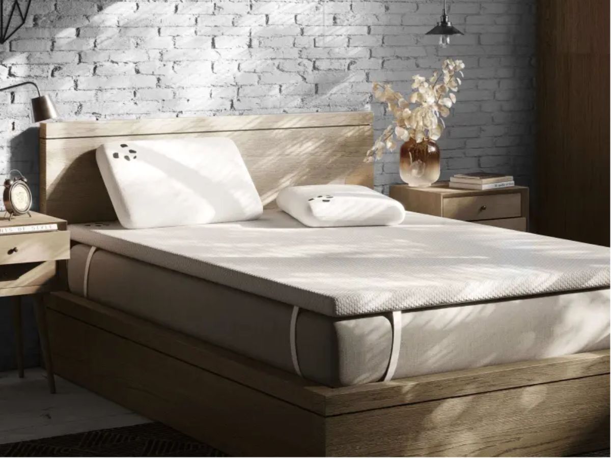 A bed with a mattress topper and two pillows.