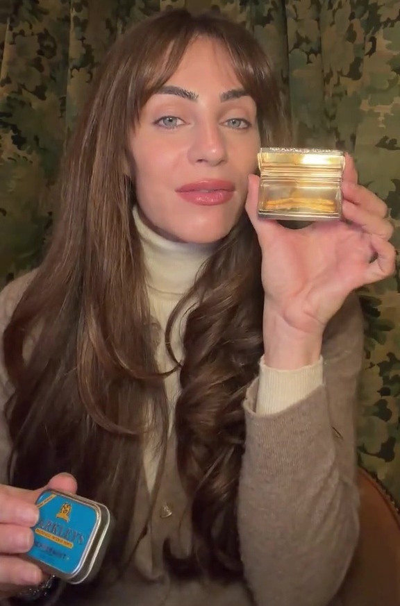 A woman holds a small silver and gold ornate box and a blue tin of mints.