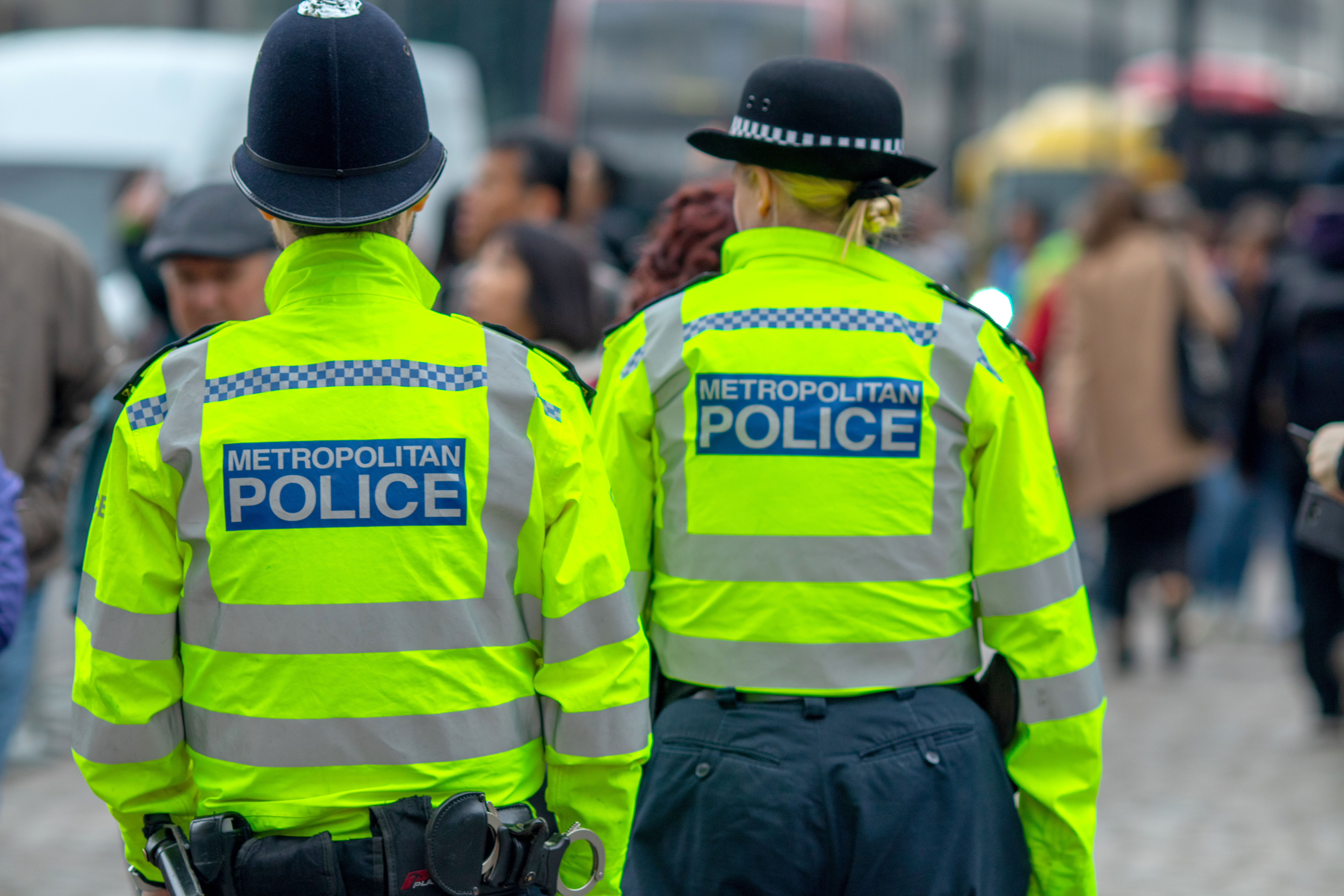 Two Metropolitan Police officers in high-visibility jackets and hats looking at crowds in Westminster, central London.