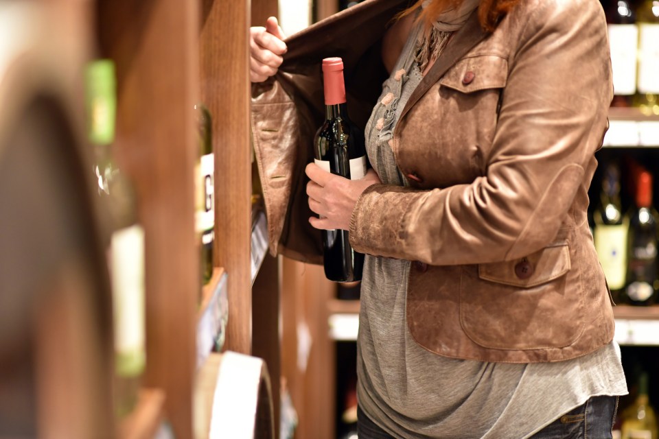 A woman stealing a bottle of wine in a supermarket.