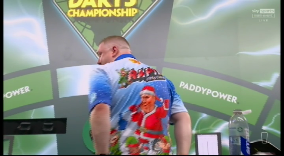 A male darts player wearing a Christmas-themed shirt with Santa Claus on it.