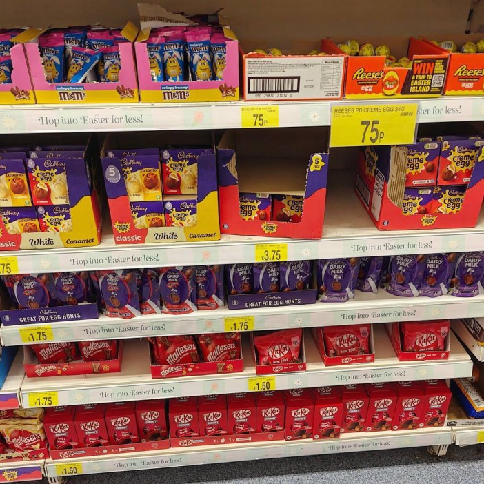 A grocery store shelf filled with Easter candy, including M&M's, Cadbury Creme Eggs, Reese's Peanut Butter Eggs, Cadbury Dairy Milk eggs, Maltesers, and Kit Kat bars.
