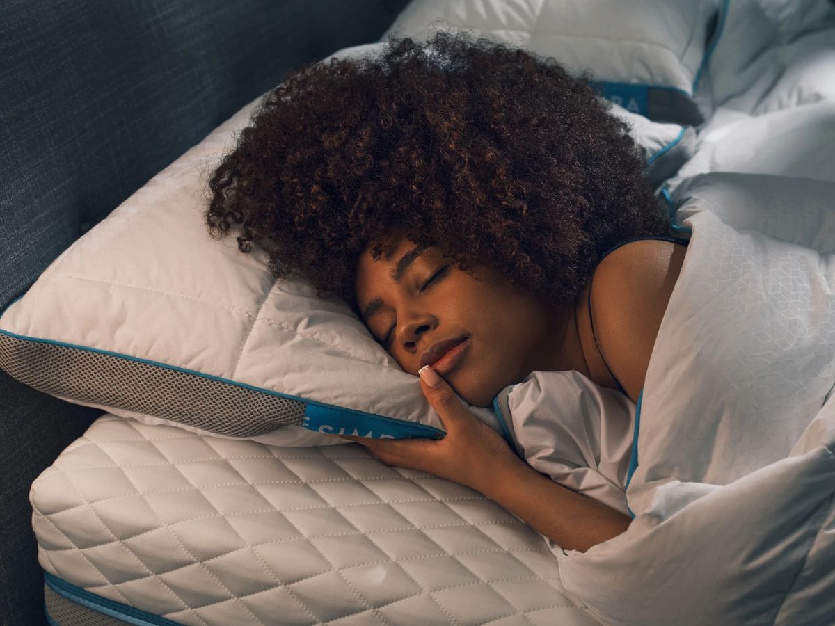 Woman with curly hair sleeping on a white pillow and mattress.