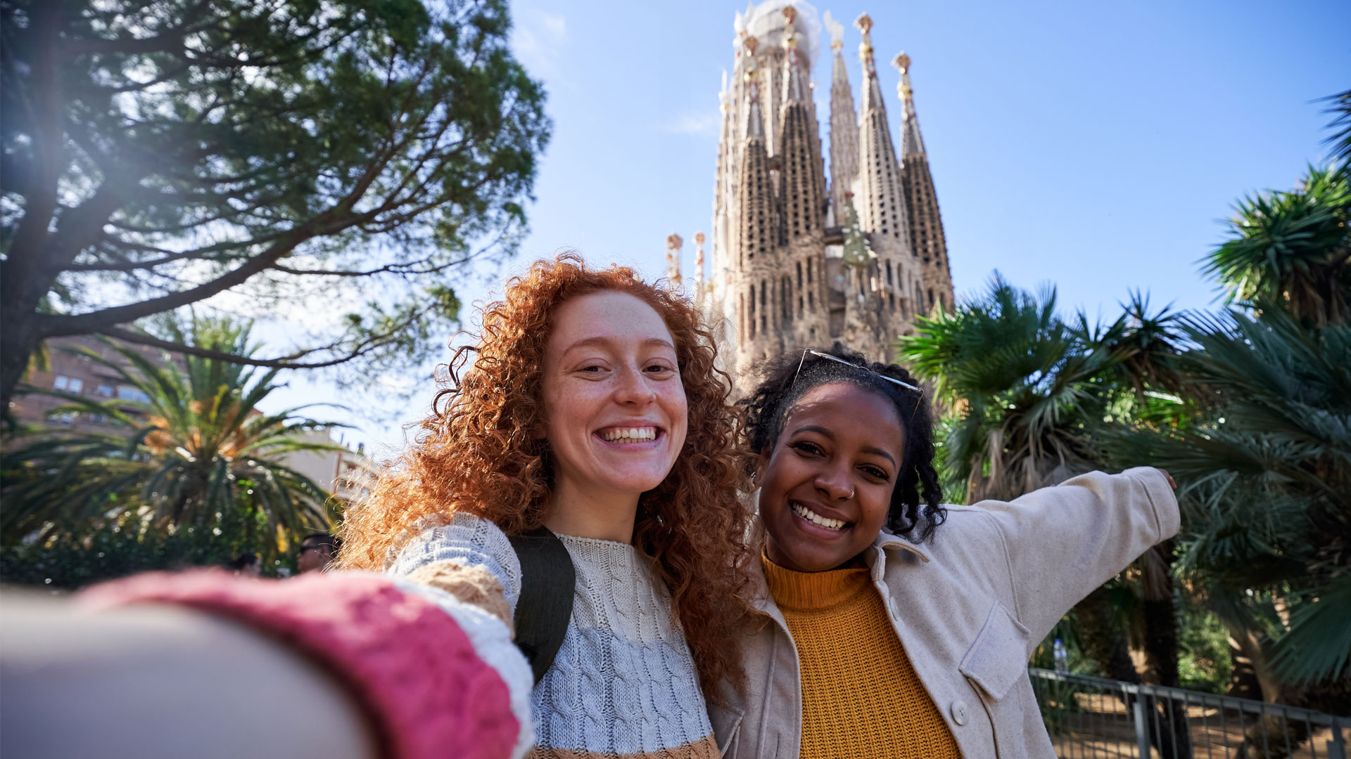 Two women smiling and posing for a selfie in front of the Sagrada Familia.