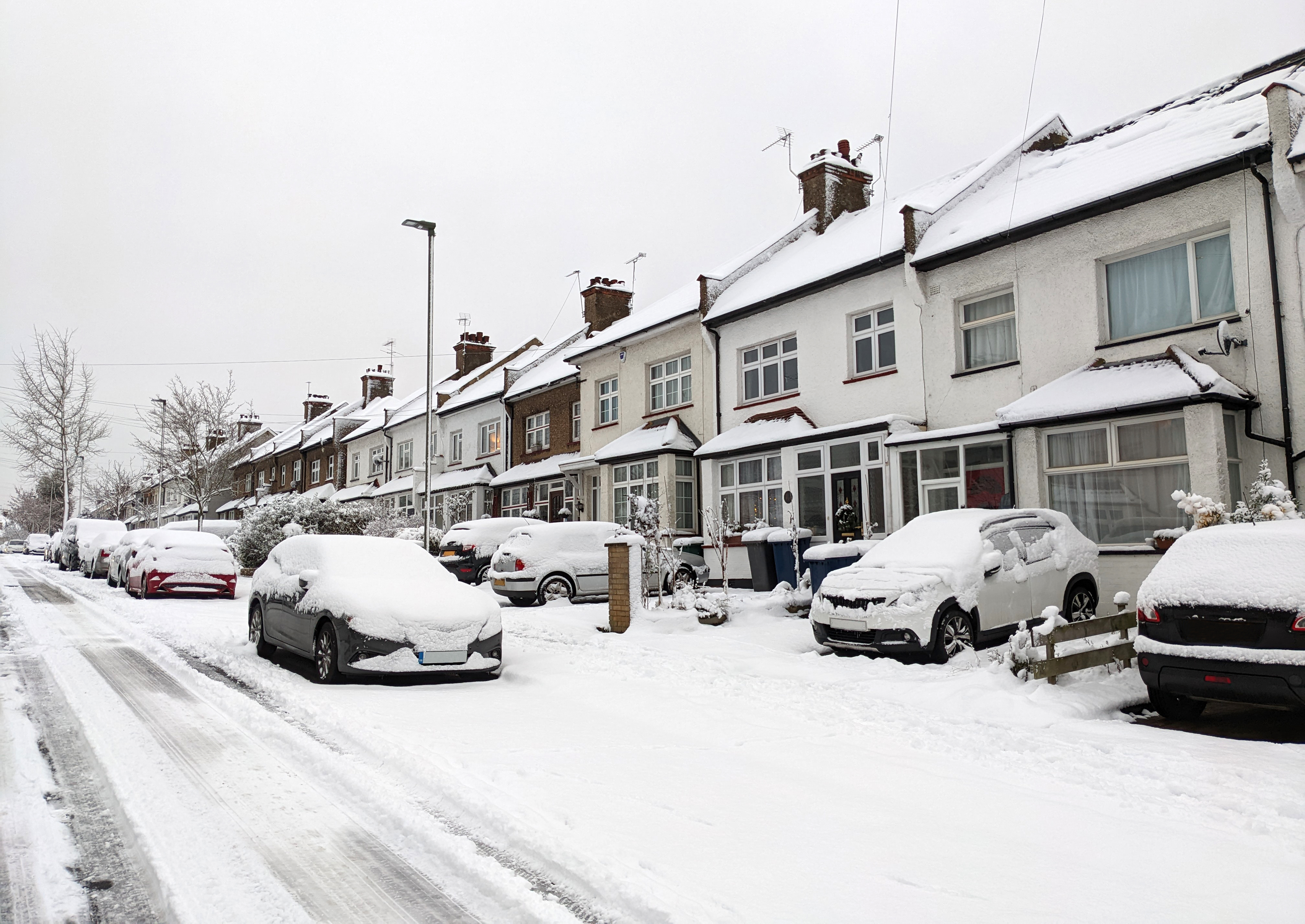 Snow covered residential street, homes and cars in North London