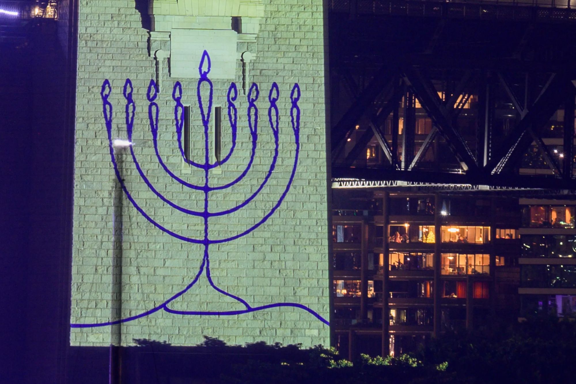 An image collage containing 1 images, Image 1 shows A menorah projected onto the pylons of the Sydney Harbour Bridge during New Year's Eve celebrations