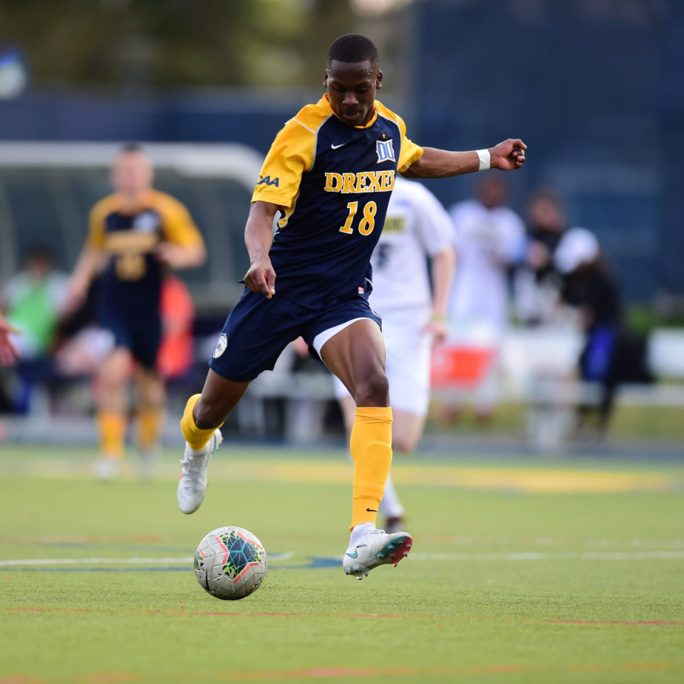 A soccer player in a blue and yellow uniform with number 18 kicking a soccer ball.