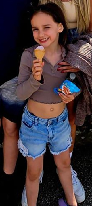 A young girl smiling while holding an ice cream cone and a snack bag.