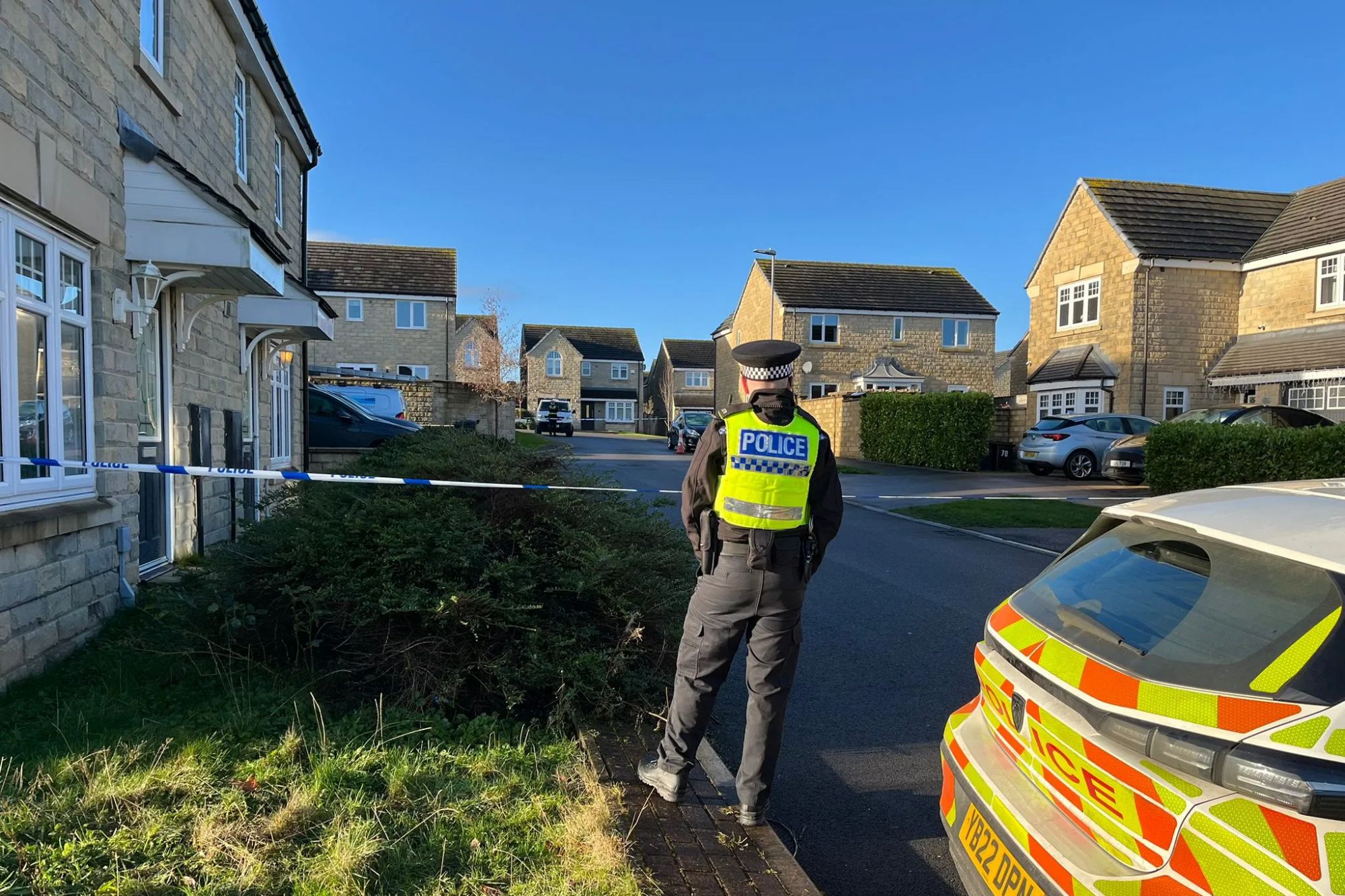 An image collage containing 1 images, Image 1 shows A police officer stands near police tape and a police vehicle in front of houses