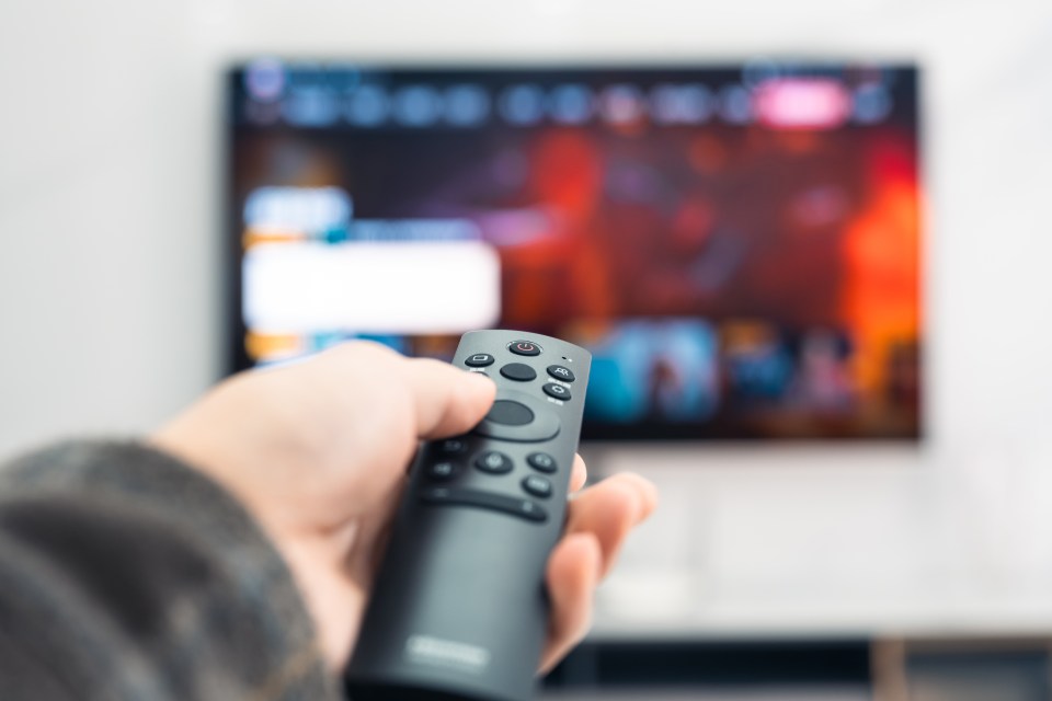 A hand holding a remote control pointed at a smart TV displaying a menu.