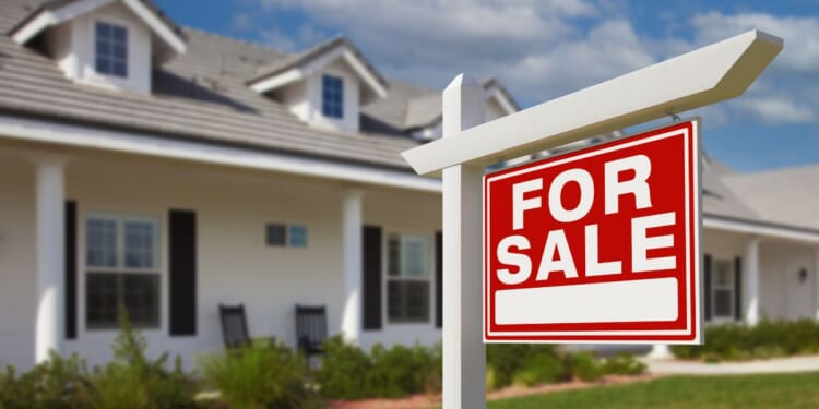 A "For Sale" sign sits on a house's front lawn.