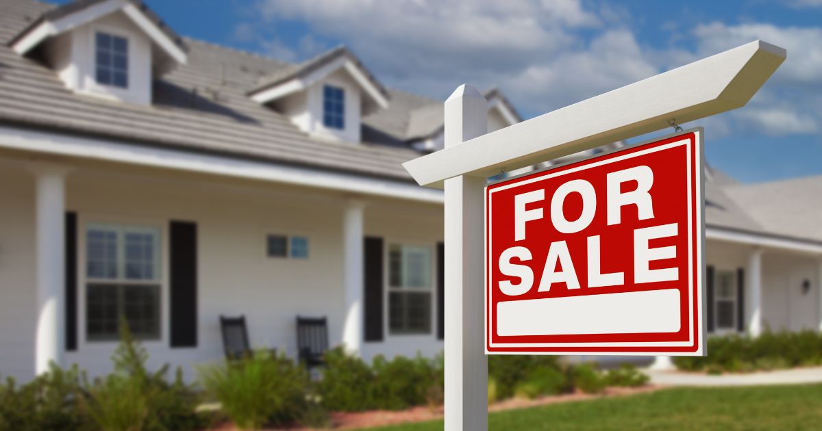 A "For Sale" sign sits on a house's front lawn.