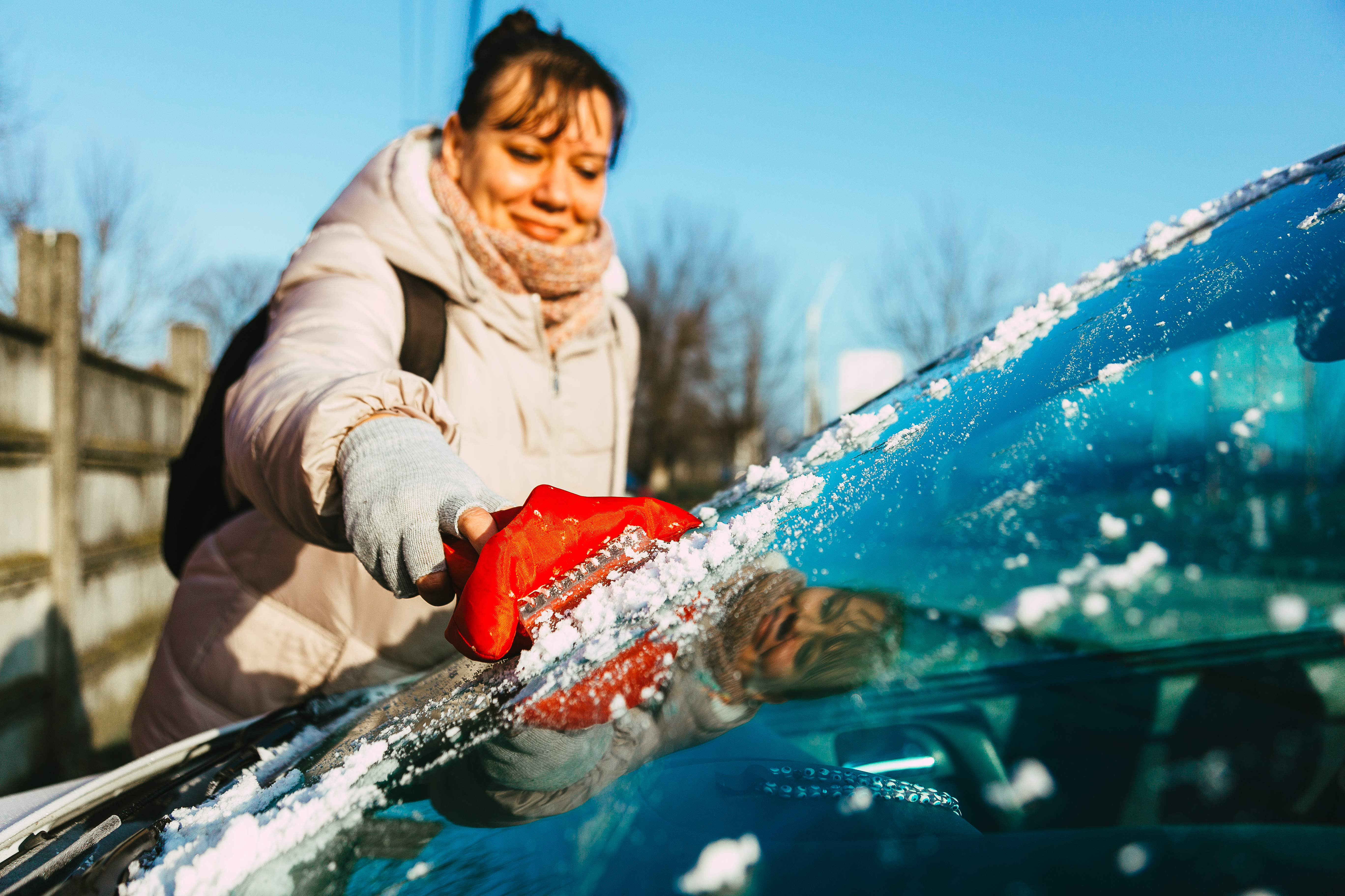 Woman scraping ice off her car windshield.
