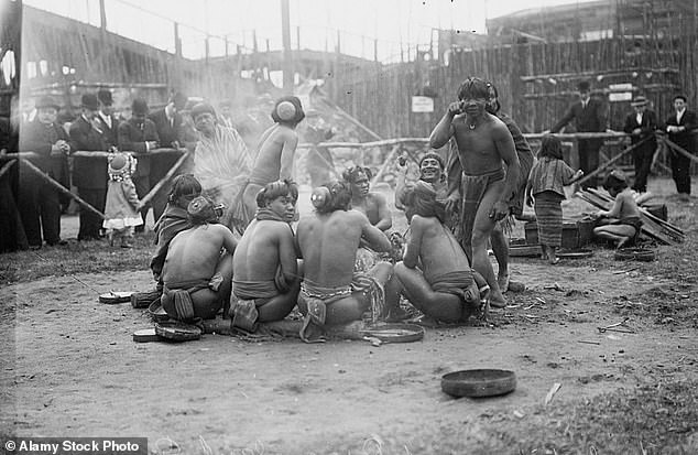 Filipinos are pictured in loin cloths sitting in a circle together at Coney Island in New York in the early 20th century while crowds of white Americans watch on from behind barriers