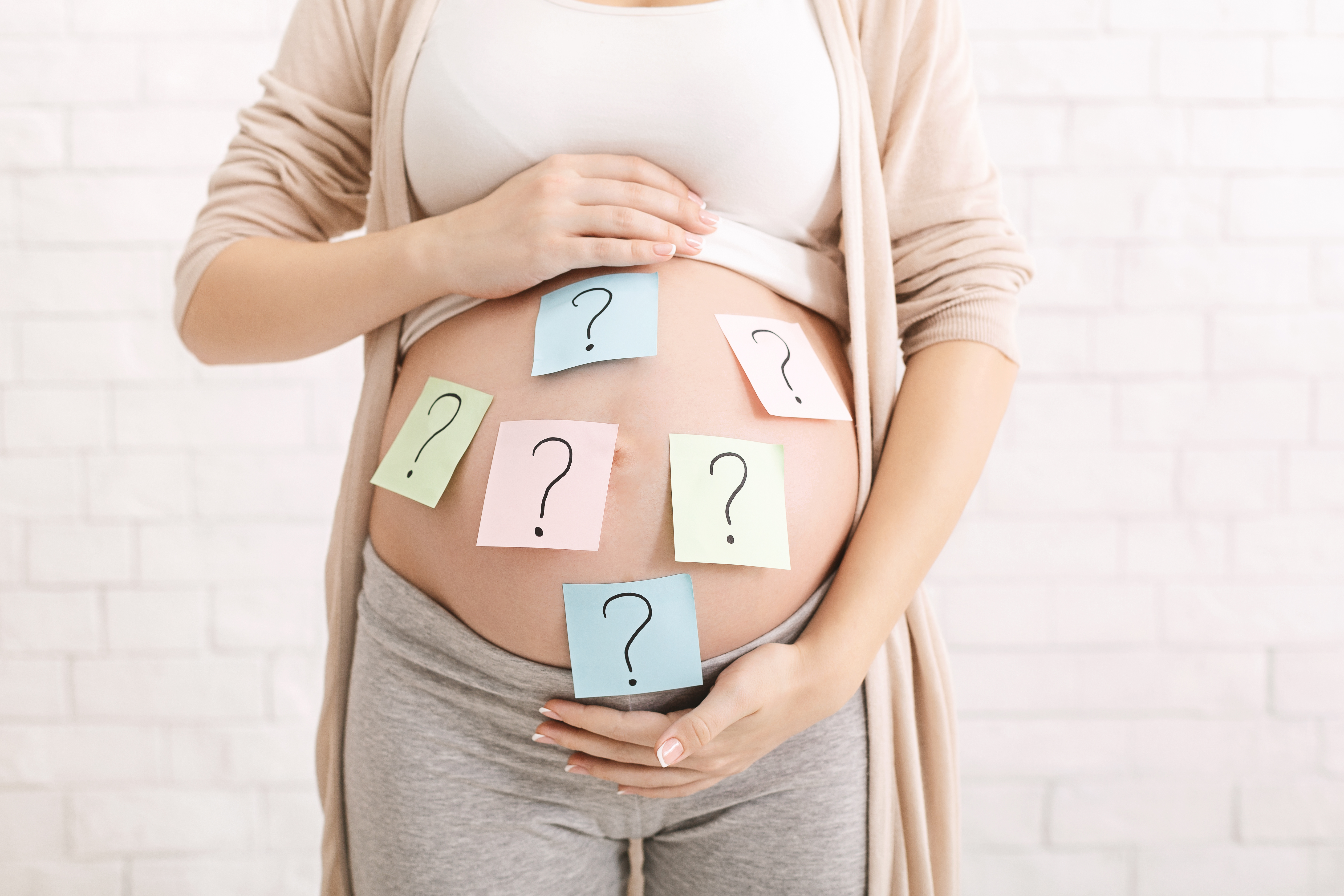 Confused pregnant woman with question marks on sticky notes on her tummy.