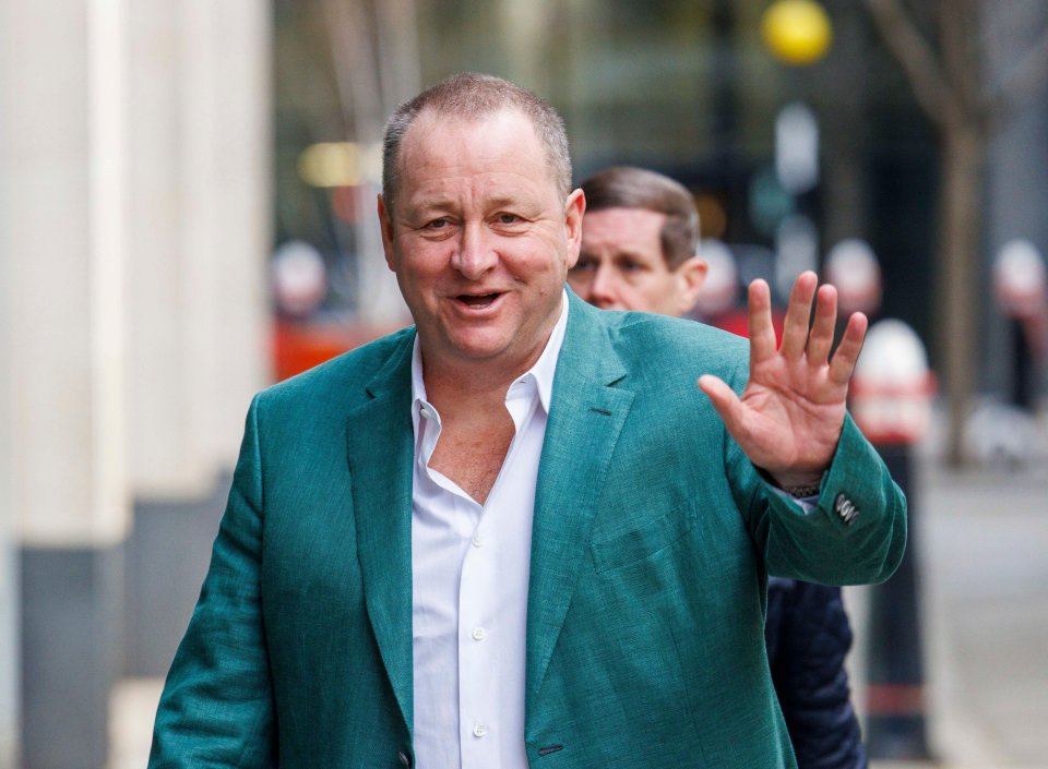 Mike Ashley, wearing a teal blazer and white shirt, waves while arriving at the High Court.