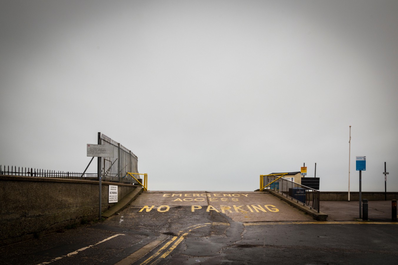 Road with "EMERGENCY ACCESS NO PARKING" painted in yellow on a gray surface, leading to an obscured horizon.