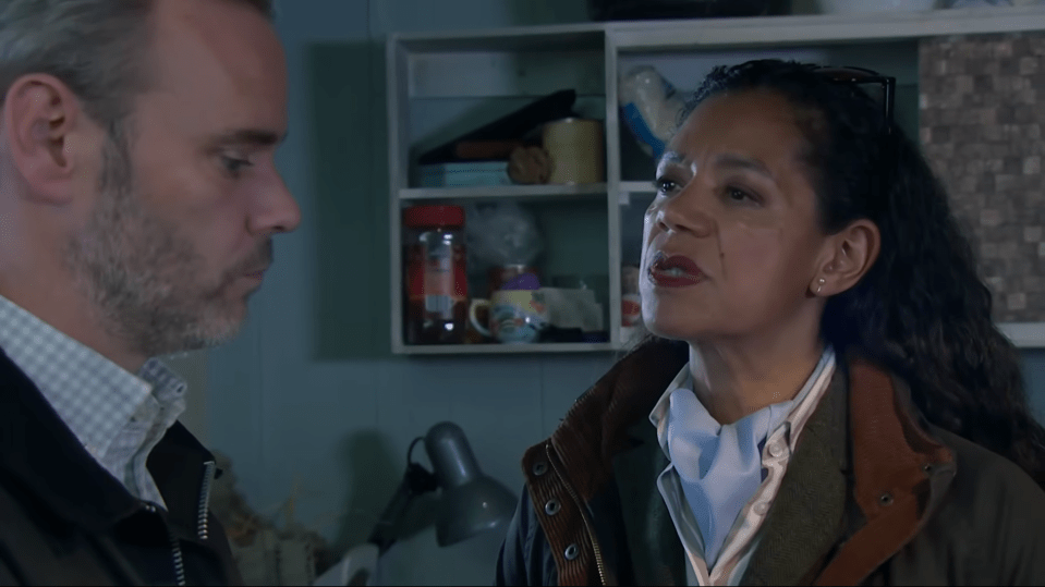 A man with a beard and a woman with dark curly hair are looking at each other.