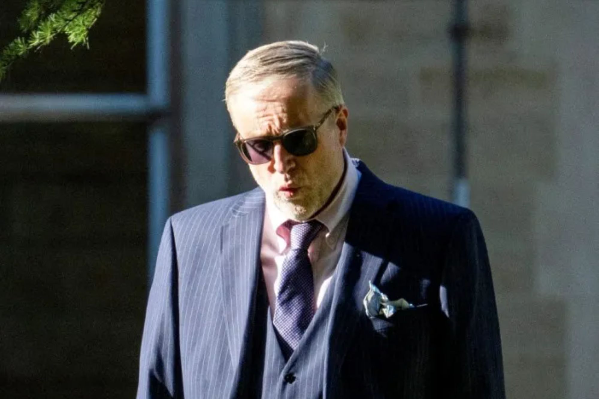 An image collage containing 1 images, Image 1 shows A man in a pinstriped suit, vest, and sunglasses walks with his hands in his pockets