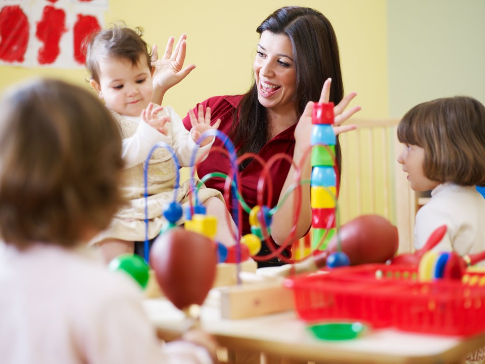 A woman playing with a baby and two young children with colorful toys.