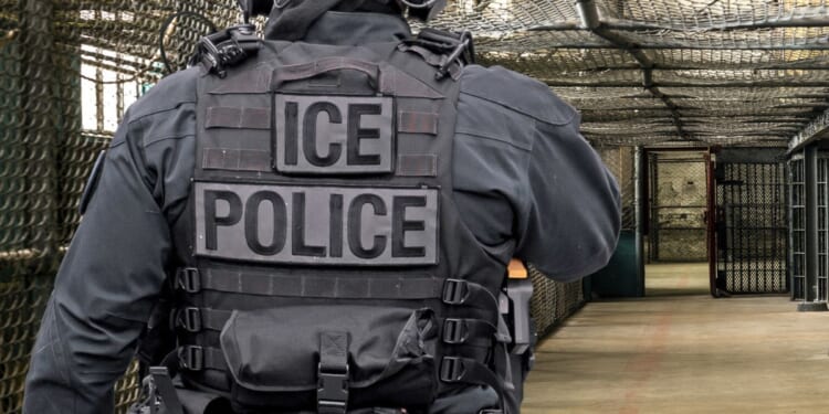 An ICE officer walks down a hall at a detention facility.
