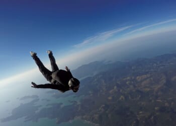 A skydiver jumps over the sea and mountains.