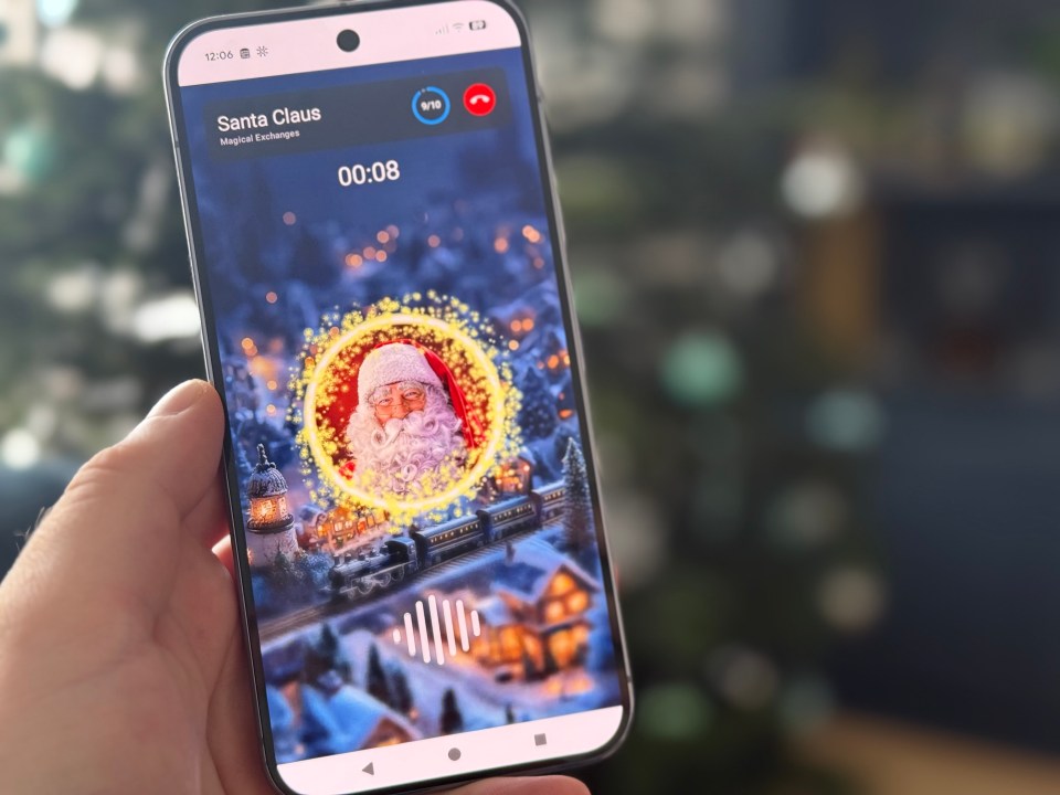 A hand holding a smartphone displaying an incoming call from "Santa Claus" with a Christmas village illustration.