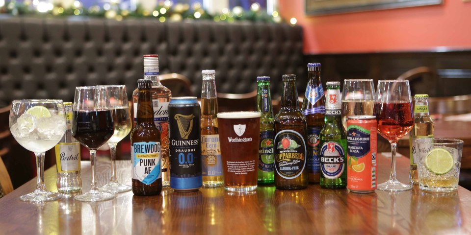 An array of bottled and canned non-alcoholic drinks on a wooden table.