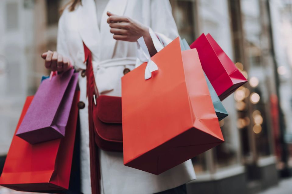 An image collage containing 1 images, Image 1 shows Woman in white coat carrying colorful shopping bags