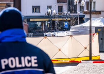 A police officer patrols on front of folding screens set up around the Constellation bar in the luxury Alpine ski resort town of Crans-Montana, on January 1, 2026 after a fire ripped through the venue during the New Year's Eve celebrations. Several dozen people are presumed dead and around 100 injured after a fire ripped through a crowded bar in the luxury Swiss ski resort of Crans-Montana, Swiss police said.