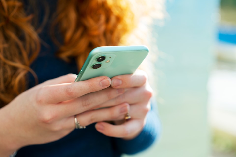 Hands of a young woman with curly red hair holding a mint green smartphone.