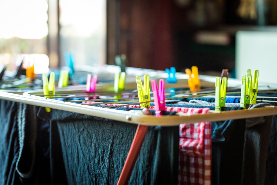 Freshly laundered clothes drying on an airer with colorful plastic pegs.