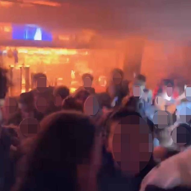 This image shows a crowd of revellers  standing in the club as the fire takes hold