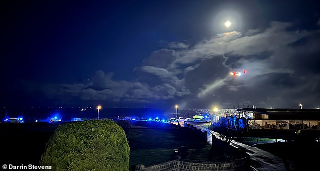 A line of blue lights flash along the sea front as the rescue operation continues