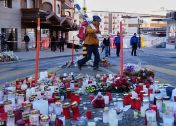 A skier passes candles near the sealed off Le Constellation bar in Crans-Montana, where at least 40 people were killed in a devastating fire during New Year's Eve celebrations