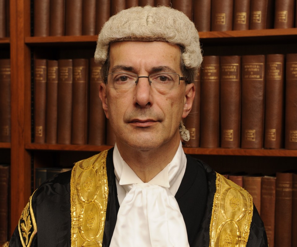 Justice Bean in his judicial robes, wig, and cravat, in front of a bookshelf.