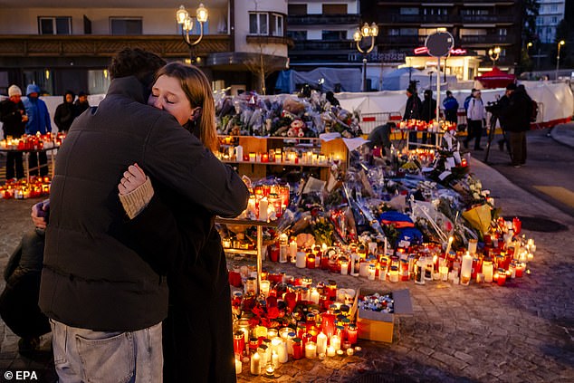 Mourners hug alongside floral tributes to the victims of the fire near the bar in Crans-Montana