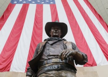 A statue of John Wayne is on display beneath an American flag in John Wayne Airport, located in Orange County, on June 28, 2020, in Santa Ana, California.