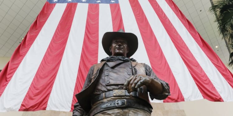A statue of John Wayne is on display beneath an American flag in John Wayne Airport, located in Orange County, on June 28, 2020, in Santa Ana, California.
