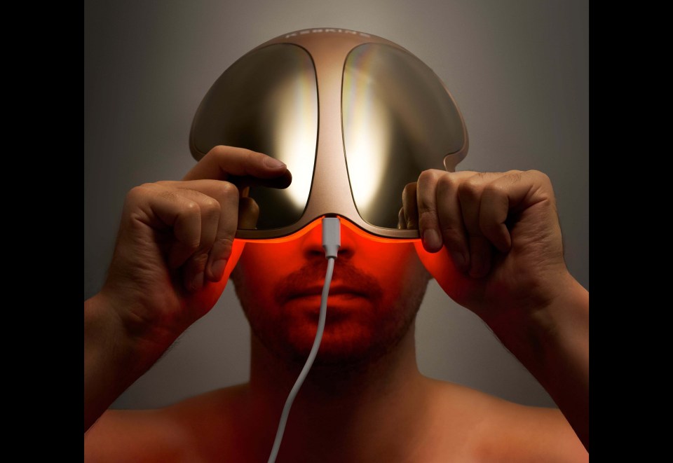 Man using a gold mask that emits red light, holding it up to his eyes.