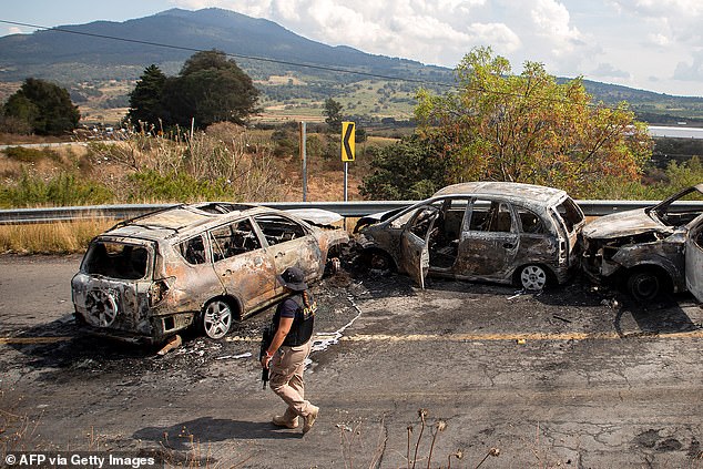 A Mexican cop patrols beside burned out cars after an attack by cartel thugs on a highway near Quiroga, Michoacan state, Mexico on Monday