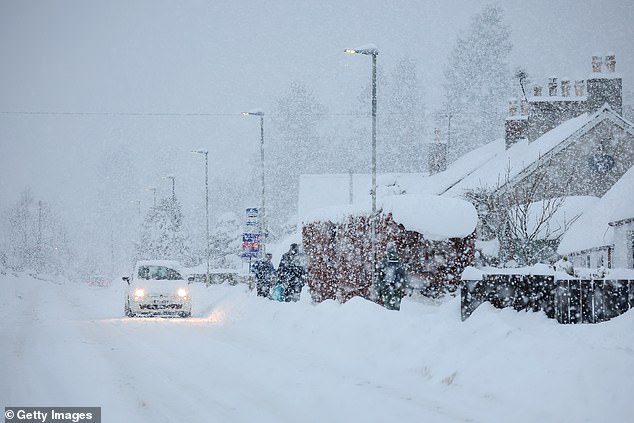 A car drives through the snow as people walk in Main Street Alford, Scotland, on Tuesday evening