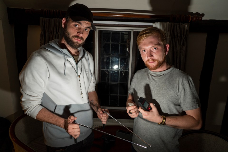 Paranormal Essex founders Adam Waughman holding dowsing rods and Robert Garey holding an EMF reader and a protection crystal.